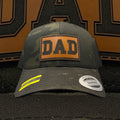 Green camouflage cap with 'DAD' patch on a textured brown and black background