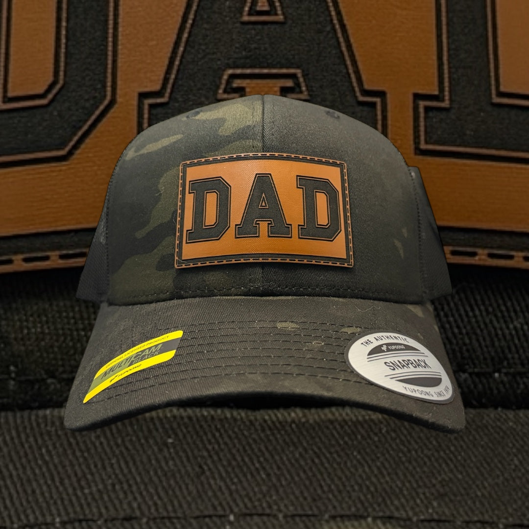 Green camouflage cap with 'DAD' patch on a textured brown and black background