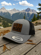 Gray cap with 'Saved by Grace' patch on a wooden surface with mountains in the background