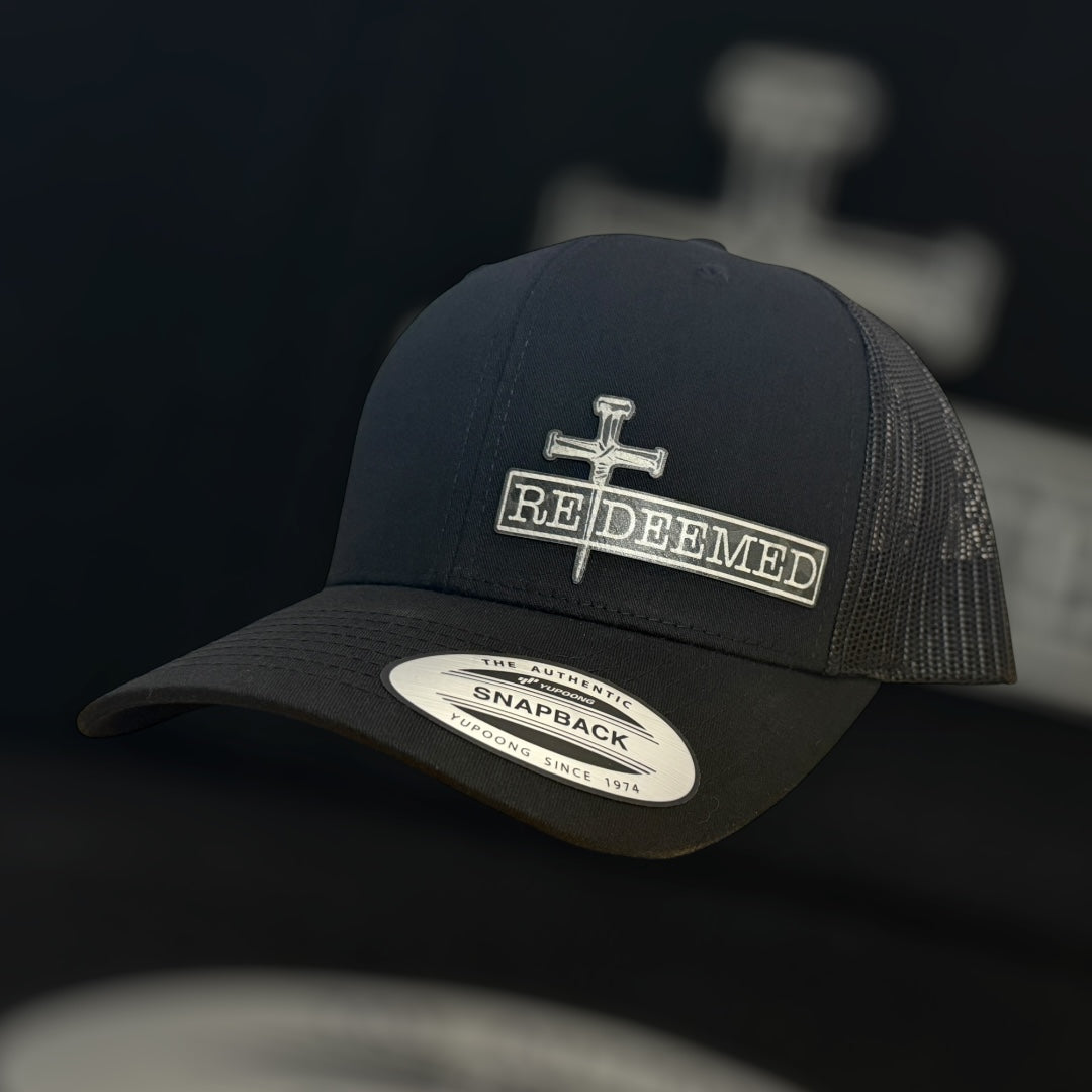 Black trucker cap with 'Re Deemed' logo on a dark background