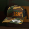 Camouflage cap with 'PAPA' patch on a dark background