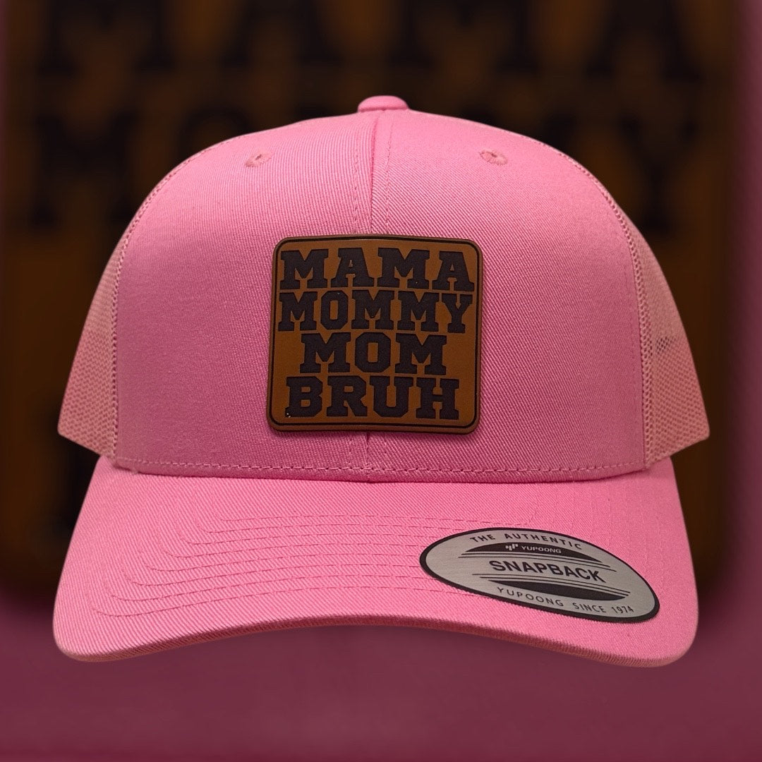 Pink cap with a brown patch reading 'MAMA MOMMY MOM BRUH' on a dark background